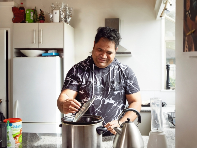 A man stands in his kitchen whilst cooking a meal.