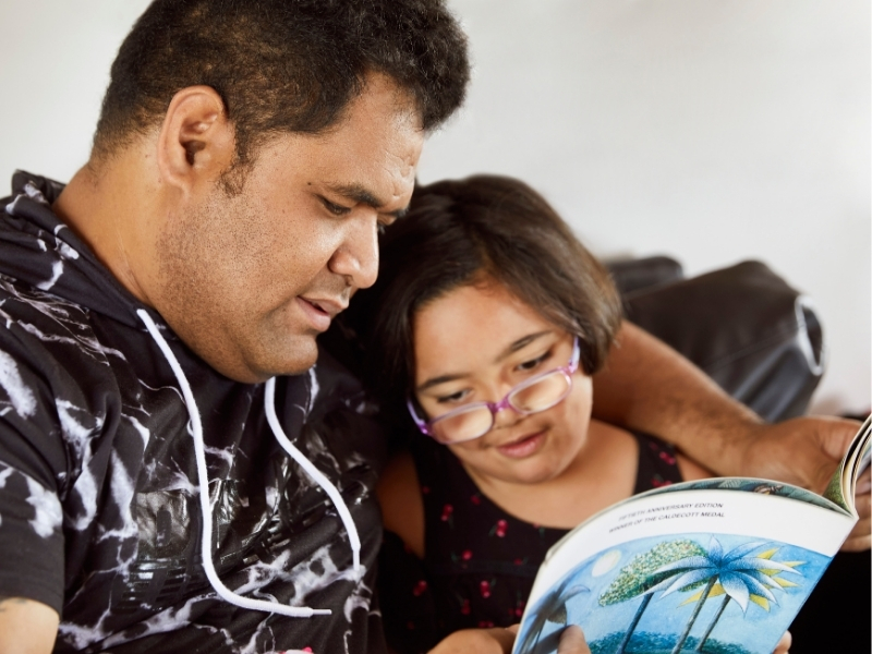 A man reads a story to his daughter whilst sitting on a couch.