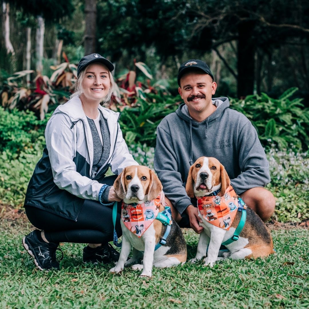 A man and a woman kneel next to their two dogs whilst on a walk through a forest.