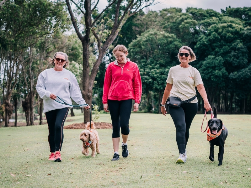 Three women walk with two dogs throughout a park