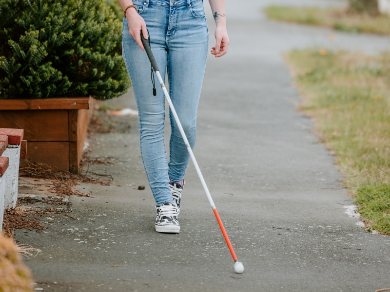 A woman walks down the street using a white cane