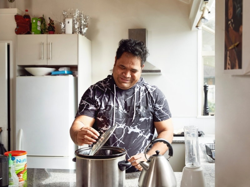 A man stands in his kitchen whilst cooking a meal.